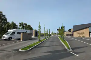 Einfahrt auf einen Campingplatz mit Wohnmobil, breiter Straße, gepflegten Wegen und Gebäuden mit Beschilderung.