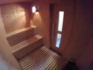Innenansicht einer Sauna mit Holzbank, Holzverkleidung und zwei Wandlampen, daneben ein Fenster im Holzrahmen.