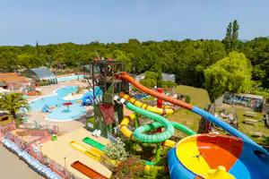 Wasserrutsche und Kinderbecken am Campingplatz, daneben Liegen, Poolbereich und Bäume im Hintergrund.
