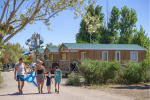 Bungalows auf einem Campingplatz, Weg und Bäume im Hintergrund, Familie mit Kindern geht am Eingang entlang.