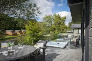 Terrasse am Campingplatz mit Whirlpool, Sitzgruppe und Tisch, daneben ein Gebäude, im Hintergrund Bäume und Hecken.
