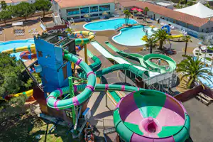 Wasserrutschen und mehrere Pools auf einem Campingplatz, mit Liegen, Palmen und einem großen Gebäude im Hintergrund.