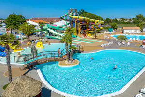 Großer Camping-Pool mit Wasserrutsche, Liegen und Sonnenschirmen, im Hintergrund Gebäude und Bäume.