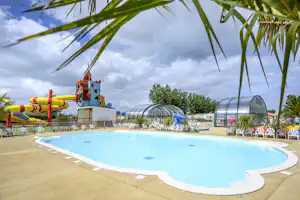 Blaues Schwimmbecken auf einem Campingplatz, daneben Spielbereich mit Hüpfburg und mehrere Gewächshaus-ähnliche Bauten.