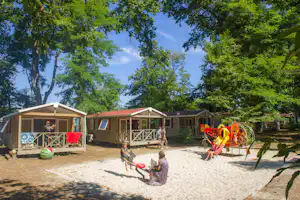 Reihe von Mobilheimen am Campingplatz mit Veranda, Kiesweg und Spielplatz mit Rutsche und Spielgeräten.