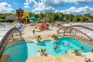 Großes Camping-Schwimmbecken mit Rutschen, Sonnenschirmen und Liegen, im Hintergrund Spielbereich und Gebäude.