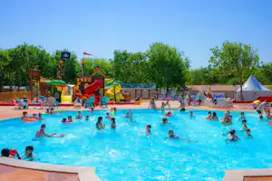 Großes Camping-Schwimmbecken mit vielen Kindern im Wasser, daneben Zelte und Spielgeräte auf dem Platz.