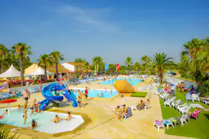 Großer Camping-Wasserpark mit Pool, bunten Wasserspielen, Liegestühlen und Palmen im Hintergrund.