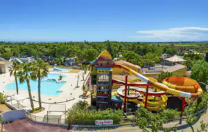 Wasserrutschen und Kinderbereich am Campingplatz neben dem Pool, mit Sonnenschirmen, Liegen und Bäumen im Hintergrund.