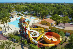 Wasserrutschen und Planschbecken auf einem Campingplatz, daneben Wohnwagen und Bungalows mit Terrassen, umgeben von Bäumen.
