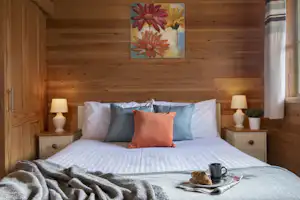 Gemütliches Schlafzimmer in einem Holzhaus: Doppelbett mit Kissen, Nachttischen, Lampen und Fenster mit Vorhang.
