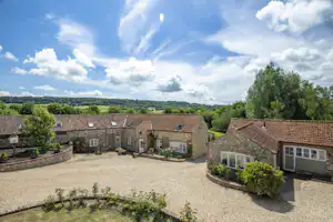 Innenhof eines Campingplatzes mit Kiesfläche, Stein-Gebäuden und Terrassen, umgeben von Bäumen und Hügeln in der Ferne.