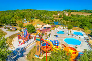 Luftaufnahme eines Campingplatzes mit Wasserrutschen, Spielbereich und mehreren Schwimmbecken, umgeben von Bäumen und Hügeln.