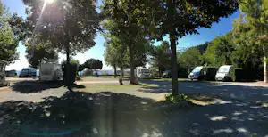 Stellplätze mit Wohnmobilen und Bäumen im Schatten, gepflasterter Weg und Rasenfläche auf dem Campingplatz.