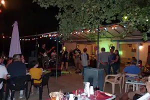 Live-Musik unter einem großen Zelt am Campingplatz, Lichterkette, Gitarrenband und Publikum auf der Terrasse bei Nacht.