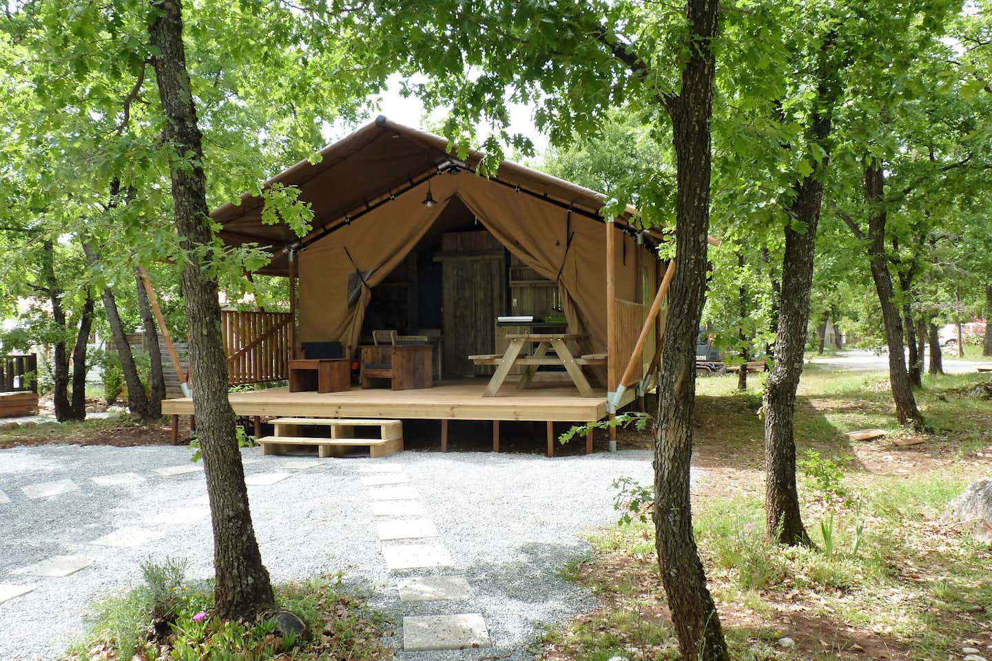 Caravaning Le Jas du Moine - Glampingzelt auf dem Campingplatz mit überdachter Veranda und Sitzgelegenheiten zwischen Bäumen
