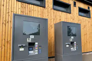 Zwei Kassenautomaten an einer Holzfassade mit grauen Gehäusen, Displays und Kartenzahlung am Campingplatz.