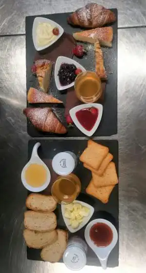 Frühstückstablett mit Croissants, Brot, Marmelade, Käse und Beeren, dazu Kaffee und Saft in Gläsern.