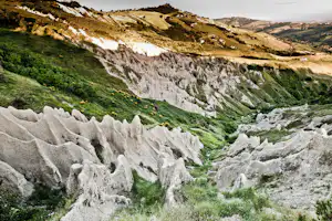 Kreidefelsen und grüne Berghänge mit Schluchten, im Hintergrund weitere Hügel und ein bewölkter Himmel.