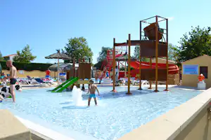 Kinderbereich im Pool mit Wasserspiel, grüner Rutsche, roten Leitern und Liegen am Campingplatz.
