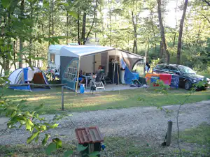 Großes Zelt mit Vorzelt auf einem Campingplatz im Wald, daneben blaue Campingstühle und ein Auto.