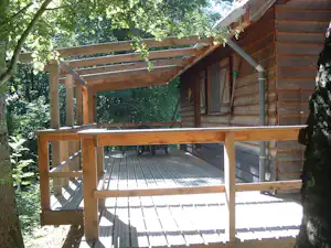 Holzveranda mit Geländer und Sitzbank am Campingplatz, umgeben von Bäumen im Grünen.