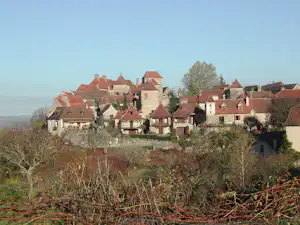 Blick auf ein Dorf mit roten Ziegeldächern und Fachwerkhäusern, umgeben von Büschen und Bäumen in der Landschaft.