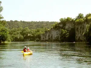 Gelbes Schlauchboot mit zwei Personen auf dem See, umgeben von Bäumen und Felswänden am Ufer.
