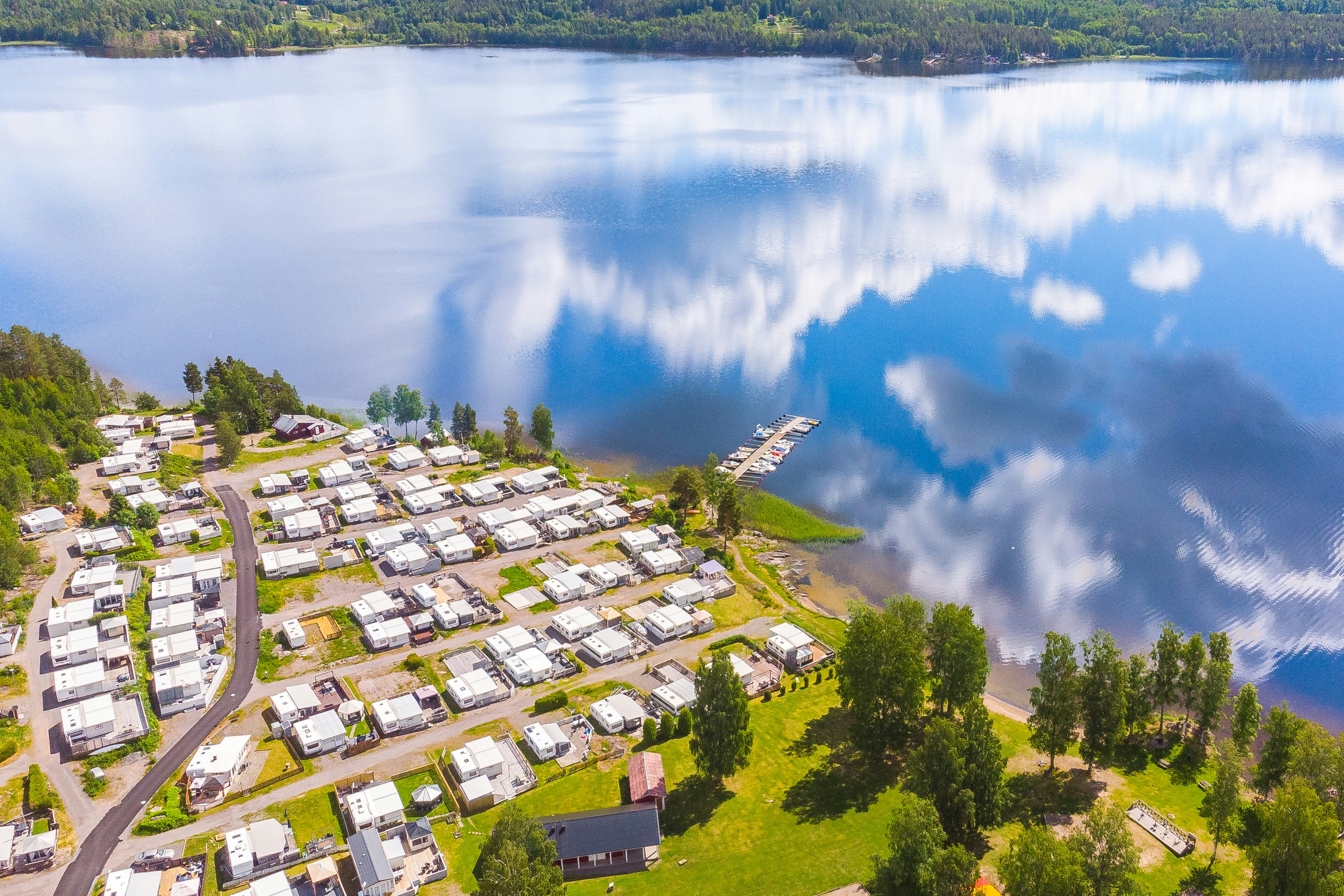 Luftaufnahme eines Campingplatzes am See mit vielen Stellplätzen, Wohnwagen und Zelten, umgeben von Bäumen und Uferlinie.