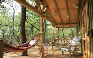 Holzveranda mit Hängematte, Sitzbank und Tisch, Blick in den Wald mit Bäumen und Holzgeländer.