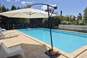 Pool auf der Camping-Terrasse mit Sonnenschirm, Liegen und blauem Wasser, umgeben von Hecken und weißem Zaun.