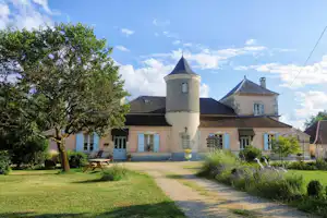Campinggebäude mit rundem Turm, Gartenweg und Rasenfläche, davor Bank und Tisch unter einem Baum.