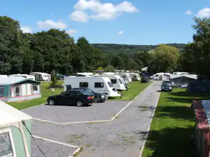 Stellplatz auf dem Campingplatz mit Wohnmobilen, einem Auto und gepflegten Wegen zwischen grünen Rasenflächen und Bäumen.