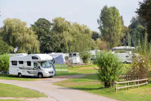 Wohnmobile auf einem Campingplatz, gepflasterter Weg und Rasen zwischen Büschen und Bäumen, im Hintergrund weitere Stellplätze.
