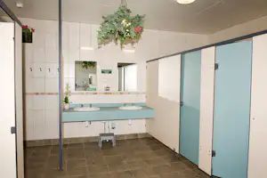 Camping-Badezimmer mit zwei Waschbecken, blauen Spinden, Fliesenboden und Spiegeln an der Wand.
