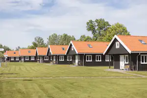 Reihe von Campinghäusern mit roten Ziegeldächern, Sitzgruppen auf Terrassen und Stühlen im grünen Rasen.