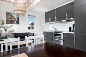 Moderne Küchenzeile mit Backofen, Kaffeemaschine und Esstisch im Wohnbereich, große Schrankfront und Fenster im Hintergrund.