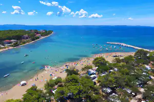 Luftaufnahme einer Bucht mit Sandstrand, vielen Booten im Wasser und einem Steg am Ufer.