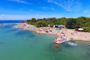 Blick auf einen Sandstrand mit vielen Sonnenschirmen, Booten am Ufer und Campingzelten im Hintergrund.