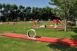 Minigolf-ähnliche Boccia-Bahn auf dem Campingplatz, rote Bahnen und Rasen, im Hintergrund Bäume und weitere Spielbahnen.