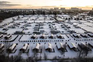 Überblick über einen Campingplatz im Winter mit vielen Wohnmobilen, Stellplätzen und Reihen von Mobilheimen auf verschneitem Gelände.