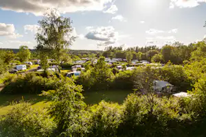Campingplatz mit Wohnwagen und Wohnmobilen inmitten von Grün, Bäumen und gepflegten Wegen zwischen den Stellplätzen.