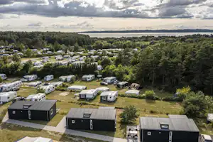 Campingplatz mit mehreren Wohnwagen und Mobilheimen auf einer Wiese, umgeben von Bäumen und Blick auf den See in der Ferne.