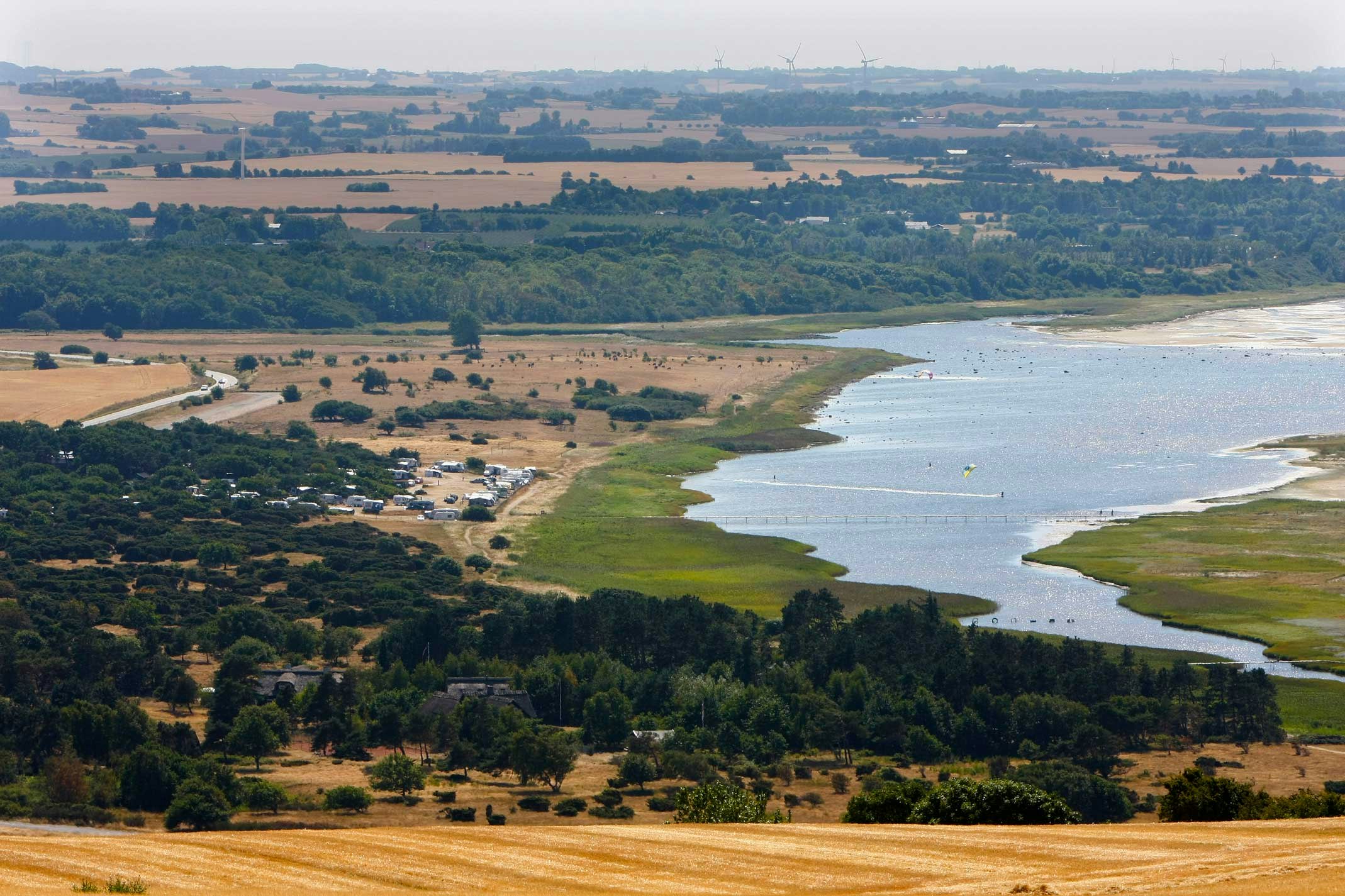 Luftaufnahme eines Flusses mit Uferstreifen und Campingplatz in der Landschaft, Felder und Wege im Hintergrund.