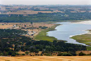 Luftaufnahme eines Flusses mit Uferstreifen und Campingplatz in der Landschaft, Felder und Wege im Hintergrund.