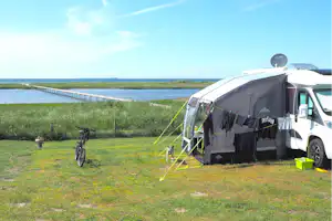 Wohnmobil mit Vorzelt und Markise auf einem Campingplatz am See, im Hintergrund Wasser und Grasfläche.