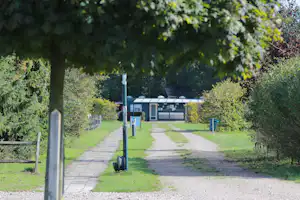 Weg im Campinggelände mit Rasen, Bäumen und einem Gebäude mit Schiebedach im Hintergrund.