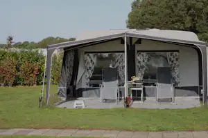 Wohnwagen mit Vordach und Terrasse, Markise geöffnet, Tisch und Stühle auf dem gepflasterten Vorplatz.