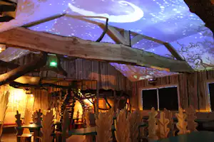 Holzdecke mit warmen Lichtern und großen Fenstern, dahinter ein beleuchteter Himmel im Innenbereich eines Campinghauses.