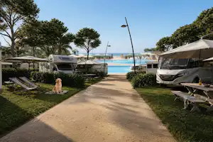 Wohnmobil und Wohnwagen auf einem Campingplatz, gepflasterter Weg zwischen Stellplätzen, Zelte und Bäume, Blick auf das Meer.